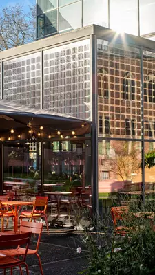 A cafe in a glass building overlooks a grassy area with outdoor seating.