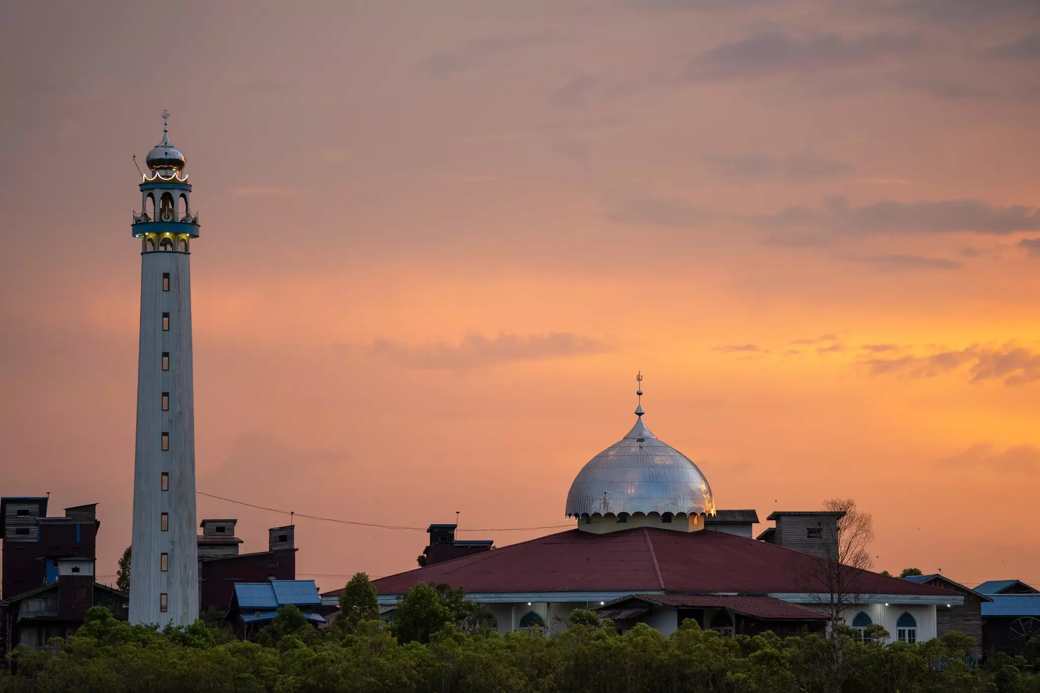 The minaret and metal dome of a mosque are seen at sunset.