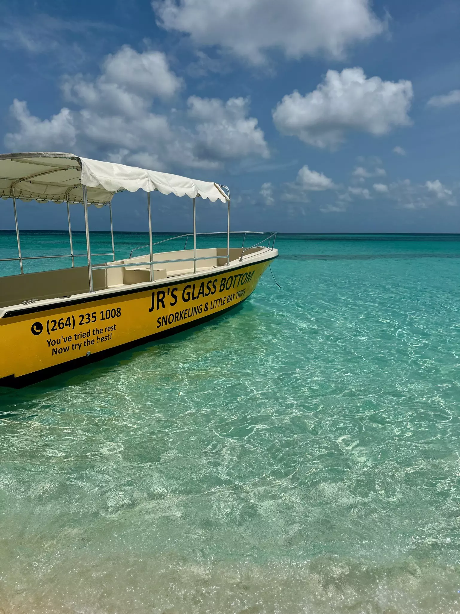 A yellow flat-bottomed boat with sunshade moored in shallow clear waters.