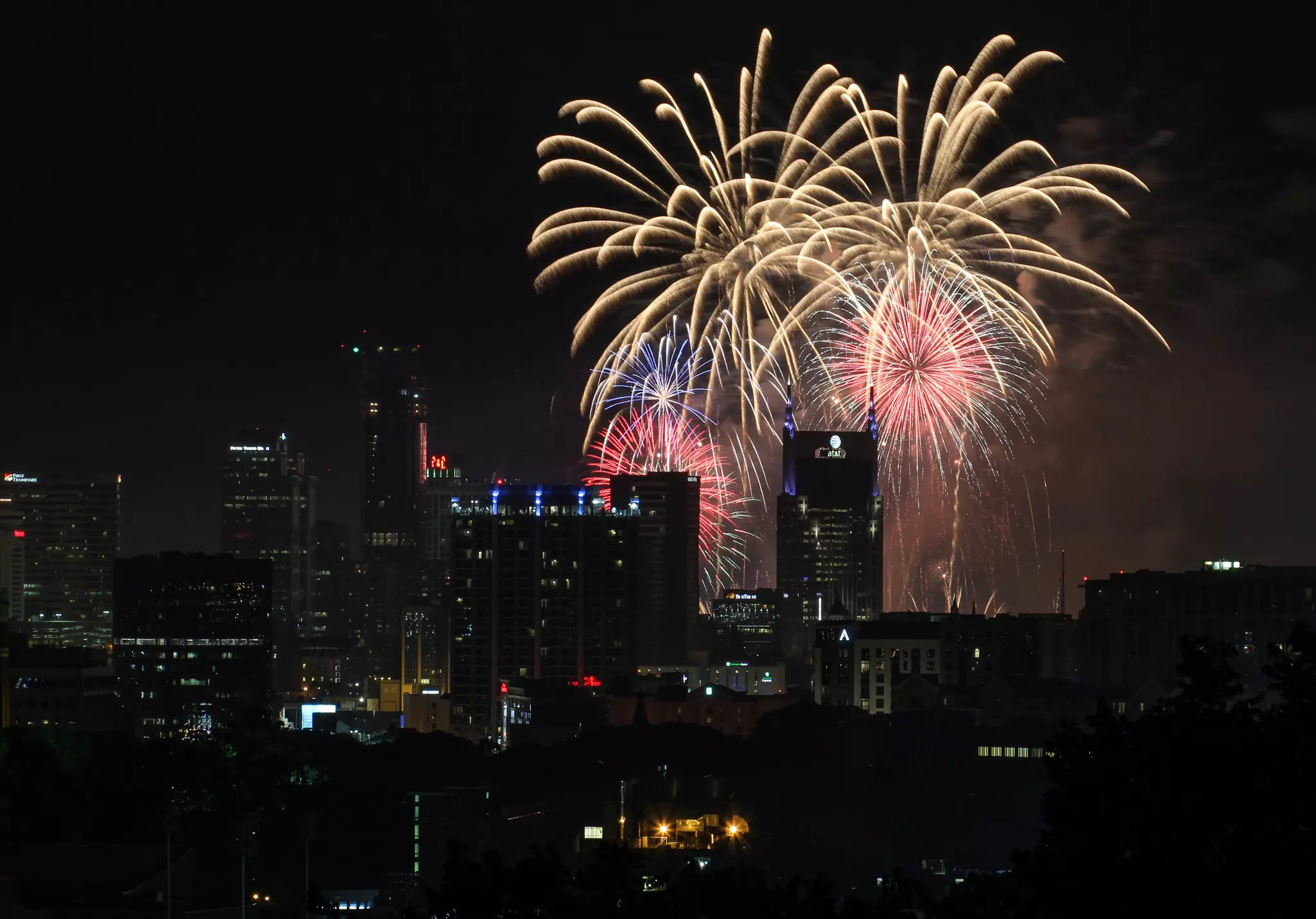 Red, white and blue fireworks in a dark sky over city buildings