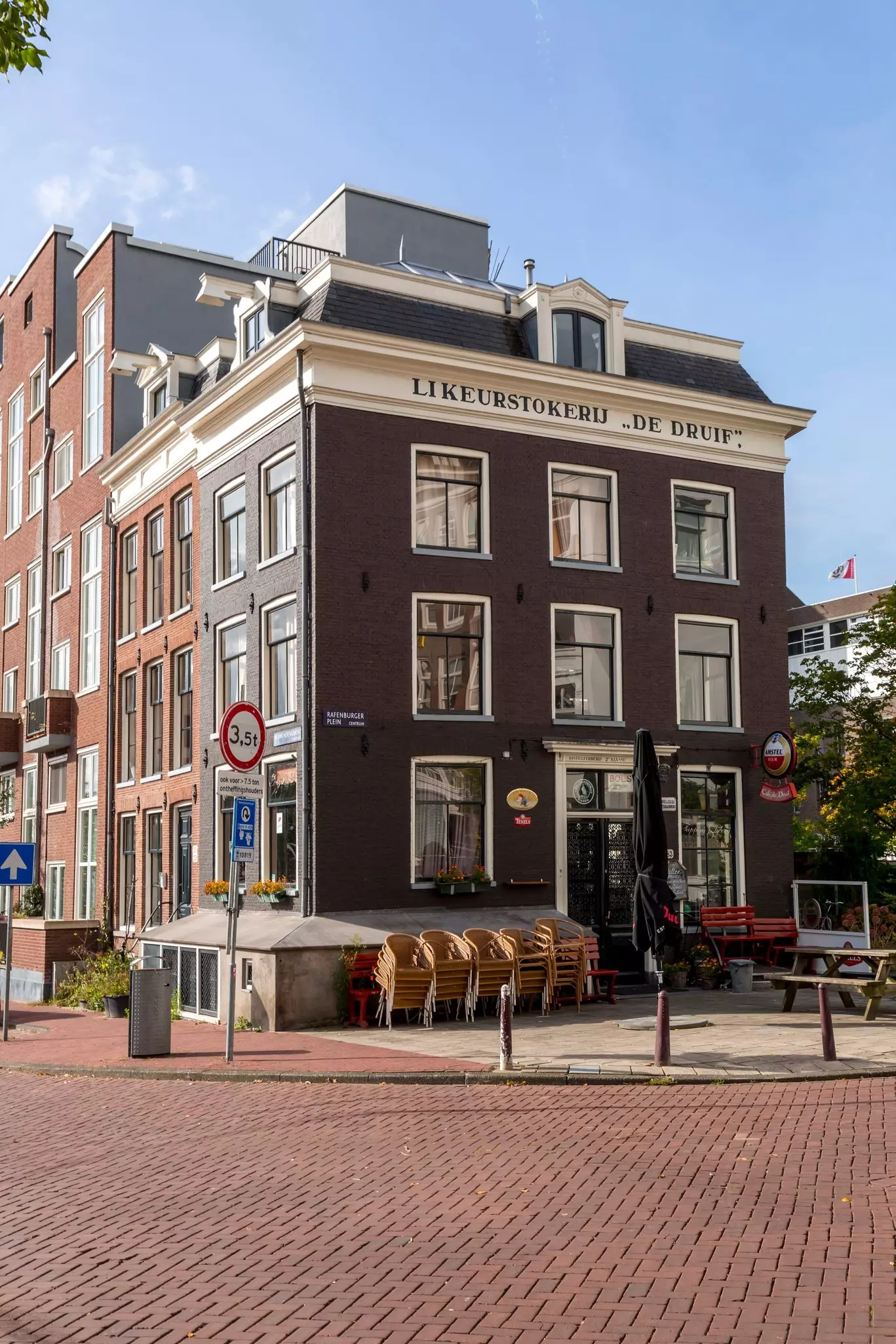 Chairs are stacked in front of a brown building on a brick-lined road