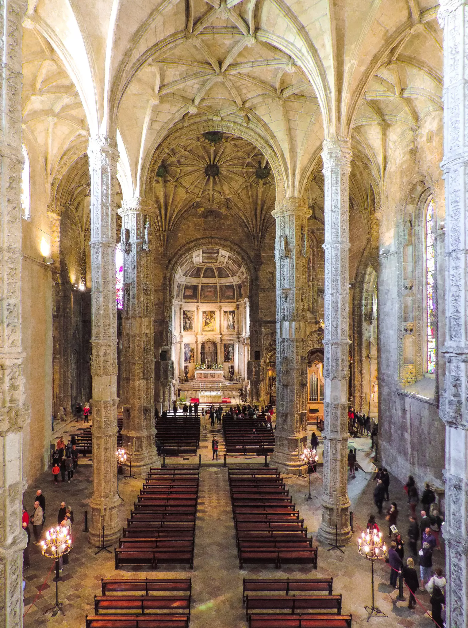 A crowd of tourists stands in front of the altar in the beautiful Mosteiro dos Jeronimos.