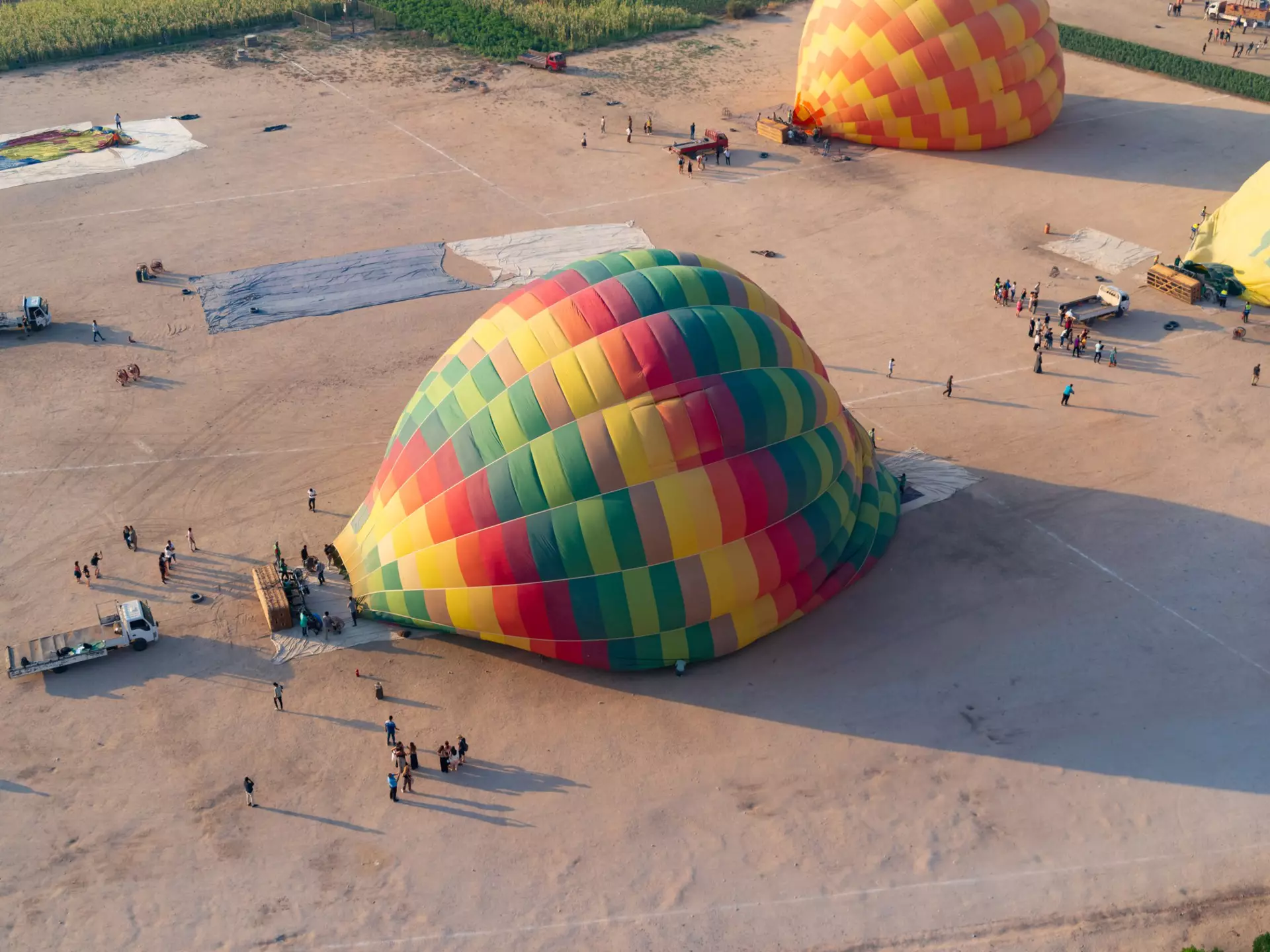 Luxor, West Bank, august 21st of 2023. The scene shows the view from inside a balloon just after taking off from the Luxor hot air balloon take off site, already above other coloured balloons that took off afterwards. The picture was taken at sunrise, while on a balloon ride over the larger area of the Valley of the Kings, part of the Theban Necropolis and a UNESCO World Heritage Site, which is a major adventure activity for visitors to Luxor, and shows the scene just below, of the balloons that were still being layed out to be filled, and others being filled with air, with the tourists and ballooning staff below on the air field. The scene shows the various stages, with some totally empty stretched on the ground, and others being filled, with the baskets turned sideways waiting for the balloon to turn the baskets as they rise, and quickly rush in the tourists for take-off.
1915670039
deir el-bahari, luxor, memorial temple, theban necropolis, unesco, valley fo the kings, attraction, balloon basket, burrial site, cables, cloudless, cloudless sky, desert, egyptian history, fertile, mortuary cult complex, mortuary temple, romantic, scenic, scenic view, shadows, sunrise, temple, tourist activity, tourist attraction, travel destination, view from above
Hot Air Balloons taking off near the Ramesseum in Luxor (III)