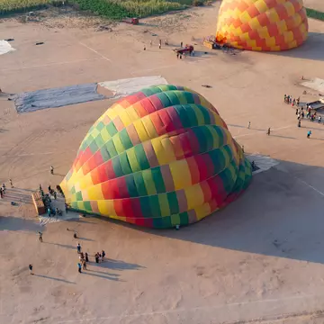 Luxor, West Bank, august 21st of 2023. The scene shows the view from inside a balloon just after taking off from the Luxor hot air balloon take off site, already above other coloured balloons that took off afterwards. The picture was taken at sunrise, while on a balloon ride over the larger area of the Valley of the Kings, part of the Theban Necropolis and a UNESCO World Heritage Site, which is a major adventure activity for visitors to Luxor, and shows the scene just below, of the balloons that were still being layed out to be filled, and others being filled with air, with the tourists and ballooning staff below on the air field. The scene shows the various stages, with some totally empty stretched on the ground, and others being filled, with the baskets turned sideways waiting for the balloon to turn the baskets as they rise, and quickly rush in the tourists for take-off.
1915670039
deir el-bahari, luxor, memorial temple, theban necropolis, unesco, valley fo the kings, attraction, balloon basket, burrial site, cables, cloudless, cloudless sky, desert, egyptian history, fertile, mortuary cult complex, mortuary temple, romantic, scenic, scenic view, shadows, sunrise, temple, tourist activity, tourist attraction, travel destination, view from above
Hot Air Balloons taking off near the Ramesseum in Luxor (III)