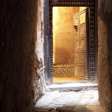 A shaded alley ends at a carved open doorway in Morocco.