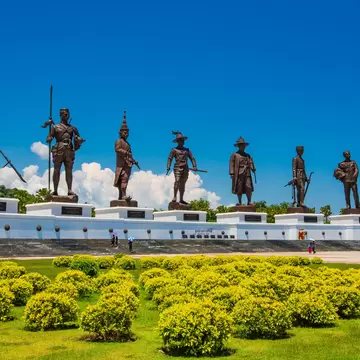 Seven giant bronze statues of Thai kings on a white plinth at Ratchaphakdi Park, Hua Hin, with clipped shrubs in front