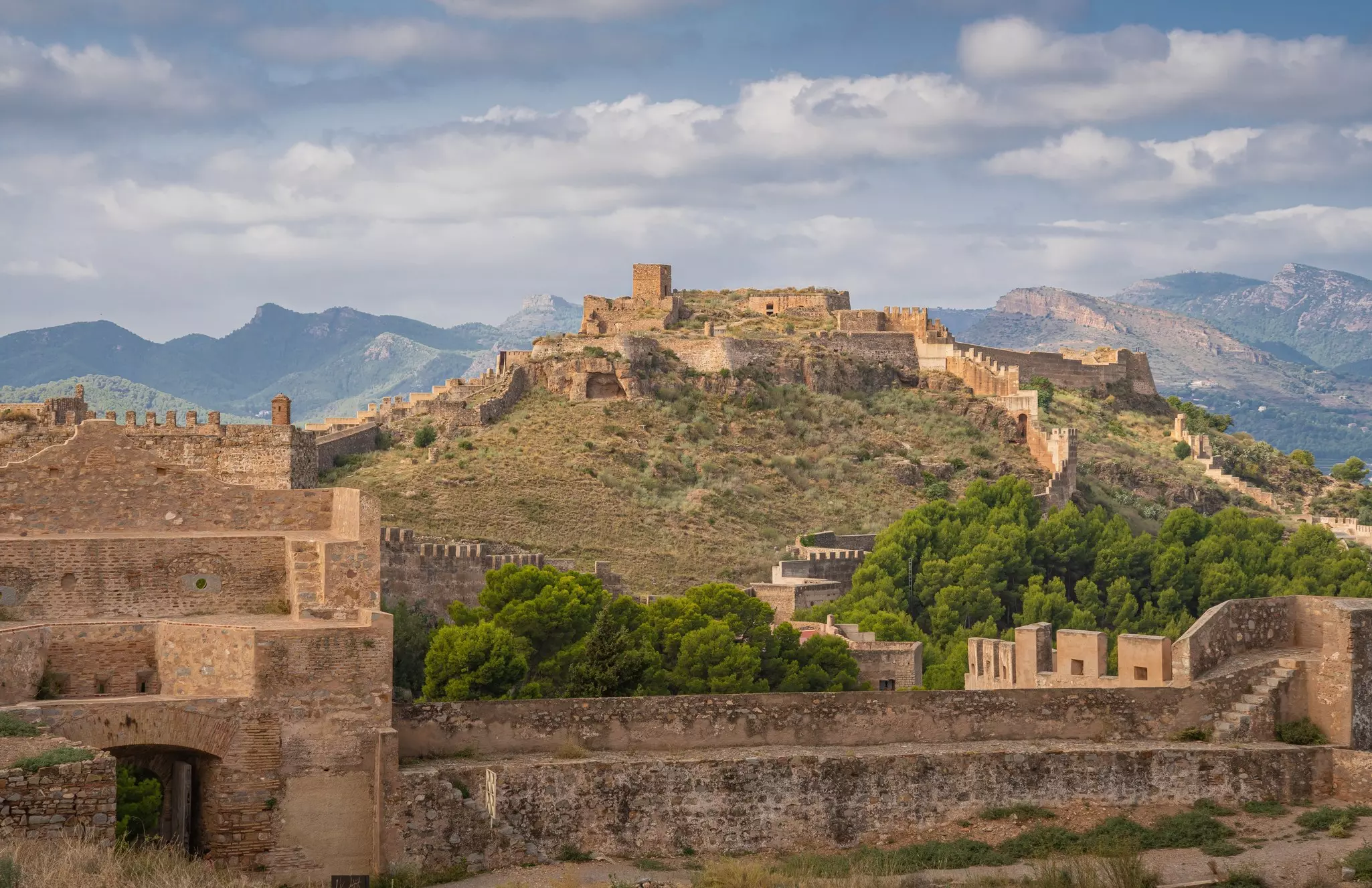A stone castle surrounded by a wall on top of a hill.