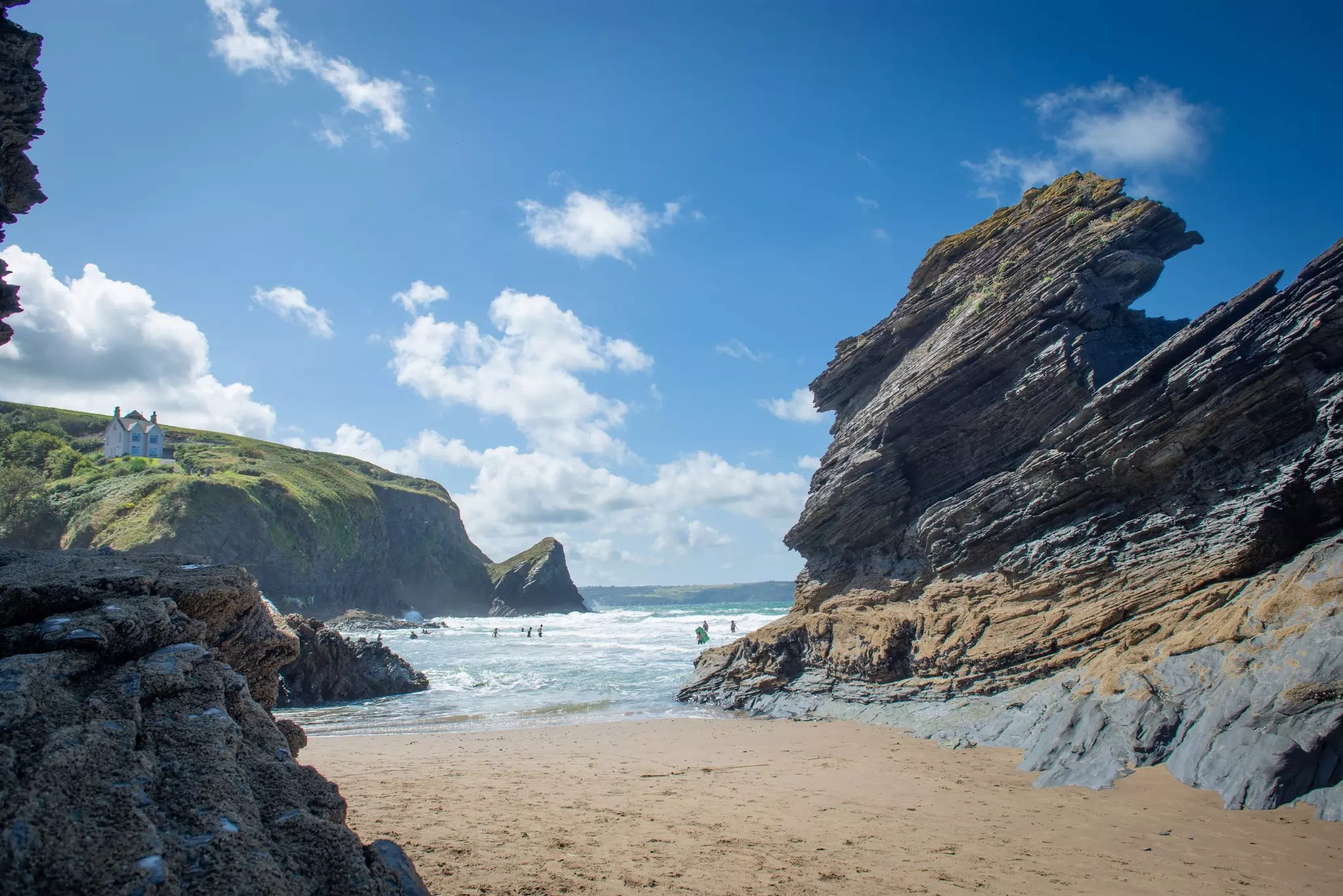 A summer's day with people on the sandy beach. Huge rock stacks and tall cliffs surround the cove.