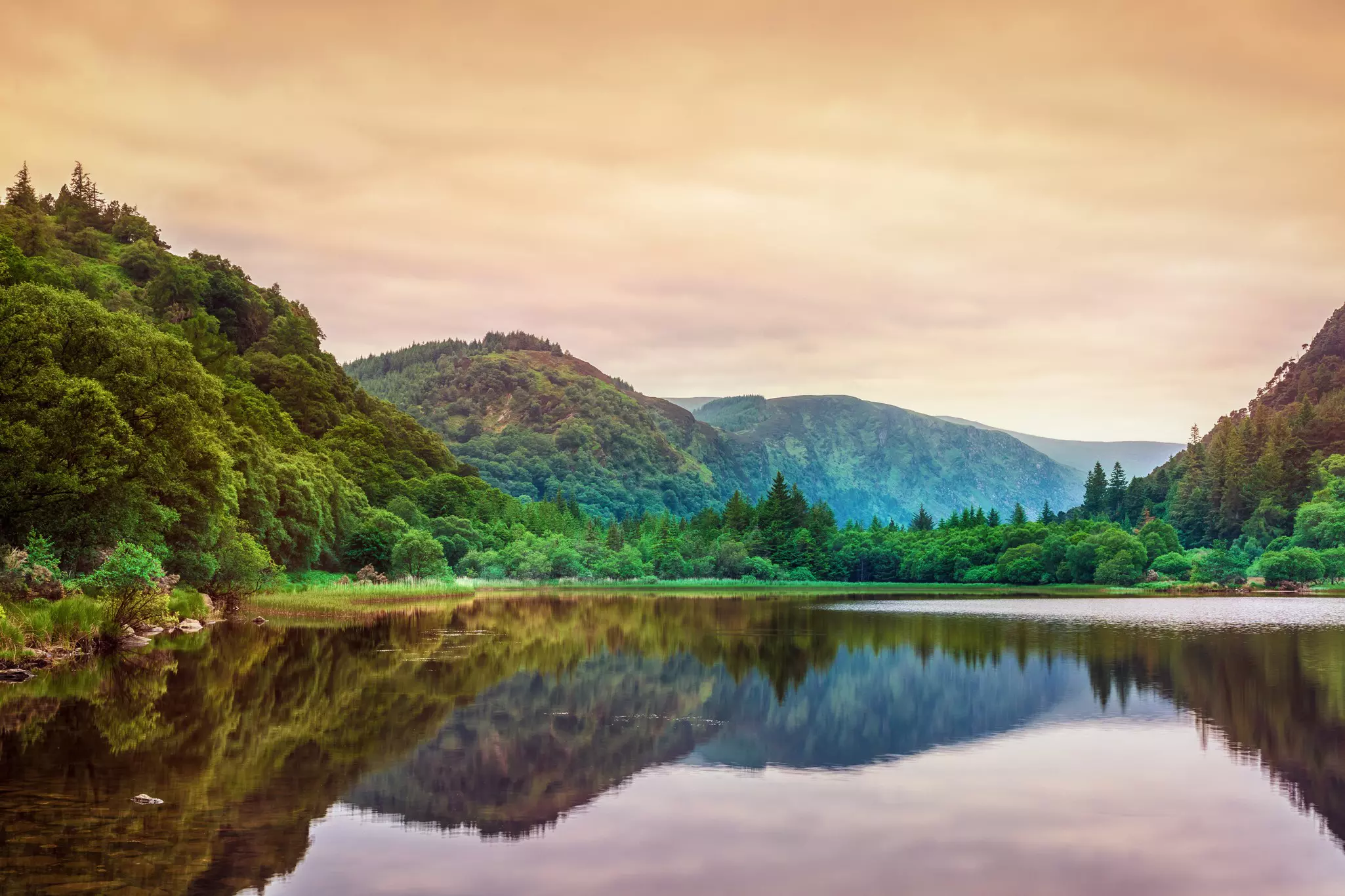 A peaceful lake reflecting the surrounding mountains in the dawn light.