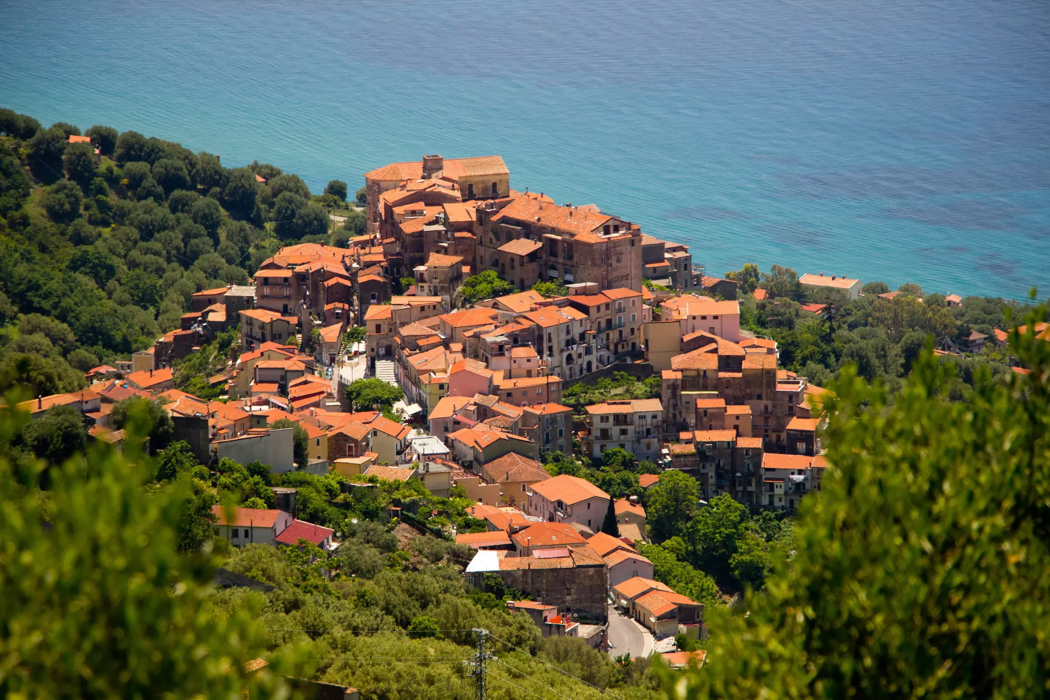 Red roofed buildings clustered together on the side of a mountain overlooking the sea