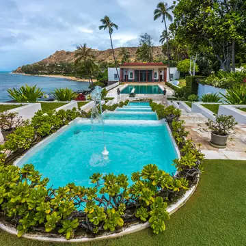 Stepped water channels leading to a pool and red-columned pavilion above the ocean