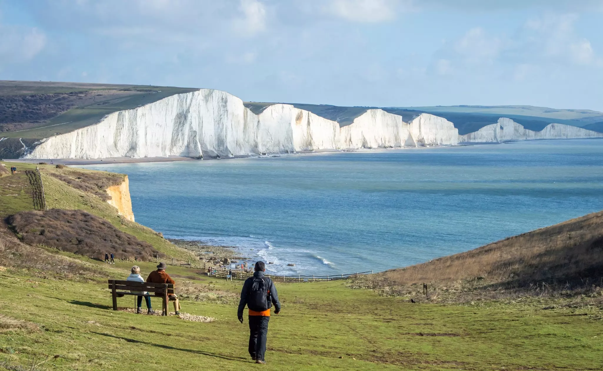 Rear view of a solo male hiker walking towards Seven Sister cliffs in a sunny day