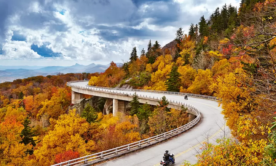 Motorcyclists ride the curving Linn Cove Viaduct through orange fall foliage on the Blue Ridge Parkway, North Carolina
