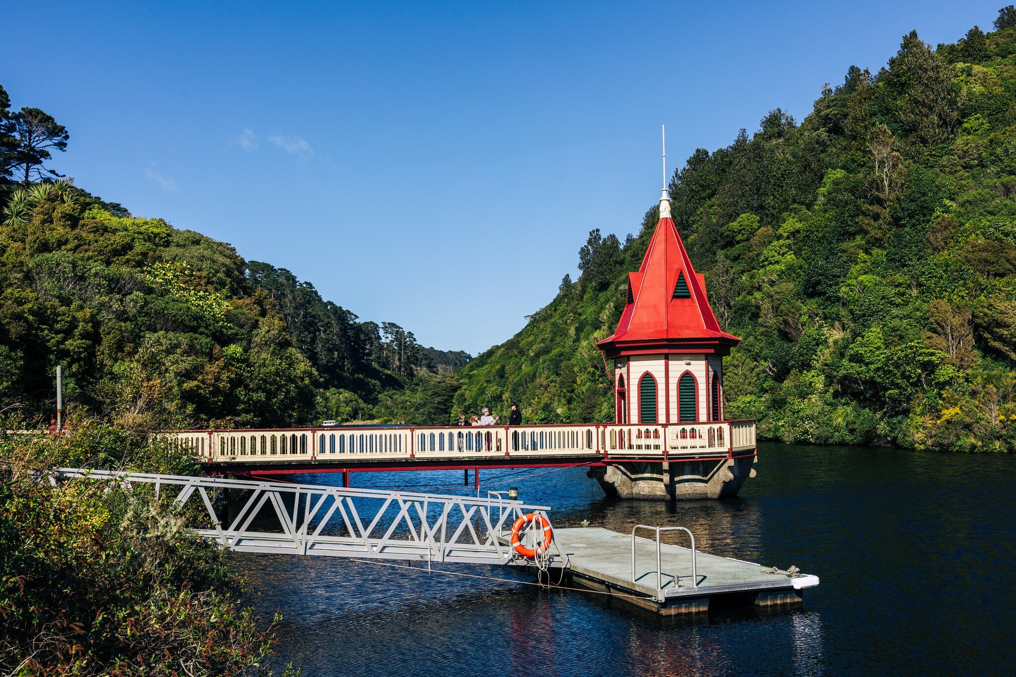 A small pier and tower with a conical red roof at the edge of a reservoir in an animal sanctuary surrounded with greenery.