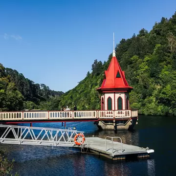 A small pier and tower with a conical red roof at the edge of a reservoir in an animal sanctuary surrounded with greenery.
