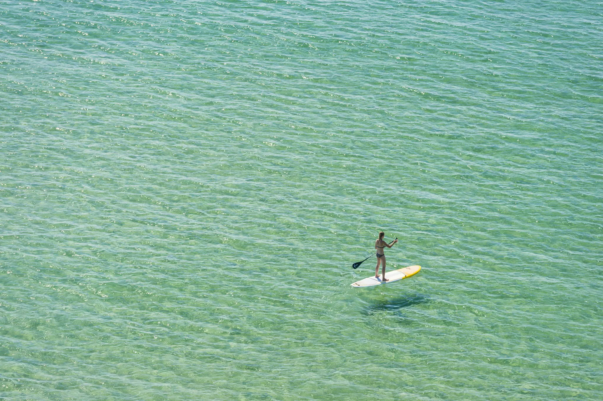 A wide shot of a woman on a stand-up paddleboard.