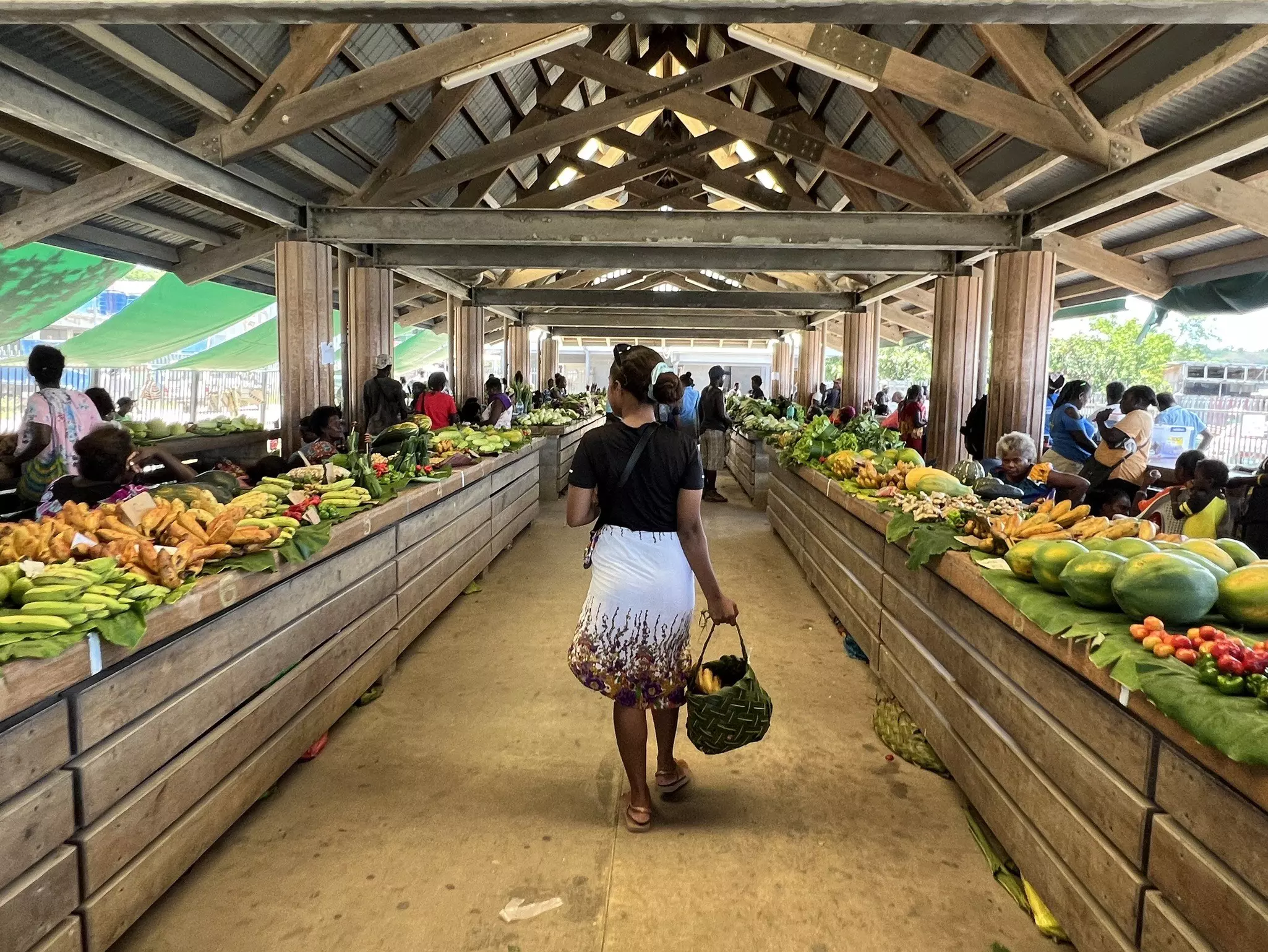 A woman, carrying a woven shopping basket, browses the fruit and vegetables on display in a covered market