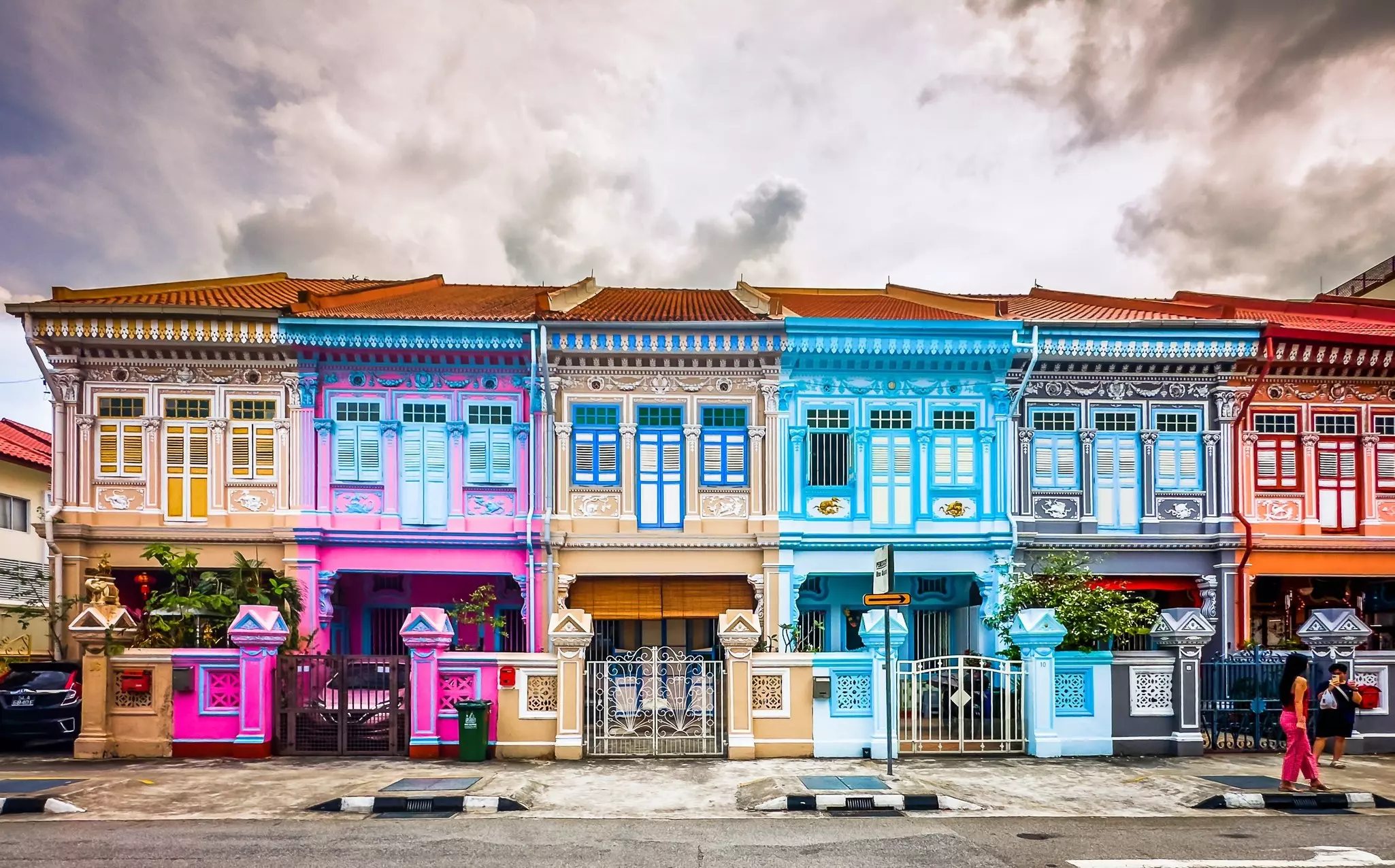 A row of historic, brightly painted houses on a city street is pictured under a stormy sky.
