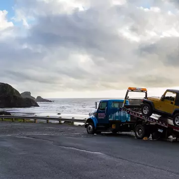 Meyers Beach, Oregon - October 27: Flat bed tow truck loading a broken vehicle with a beautiful coastal landscape in the background. October 27 2016, Meyers Beach, Oregon., License Type: media, Download Time: 2025-11-11T18:32:27.000Z, User: meg3348277, Editorial: true, purchase_order: 56530 - Guidebooks, job: Global Publishing-WIP, client: Lonely Planet 'Journey - Pacific Coast Highway 1', other: Megan Cassidy