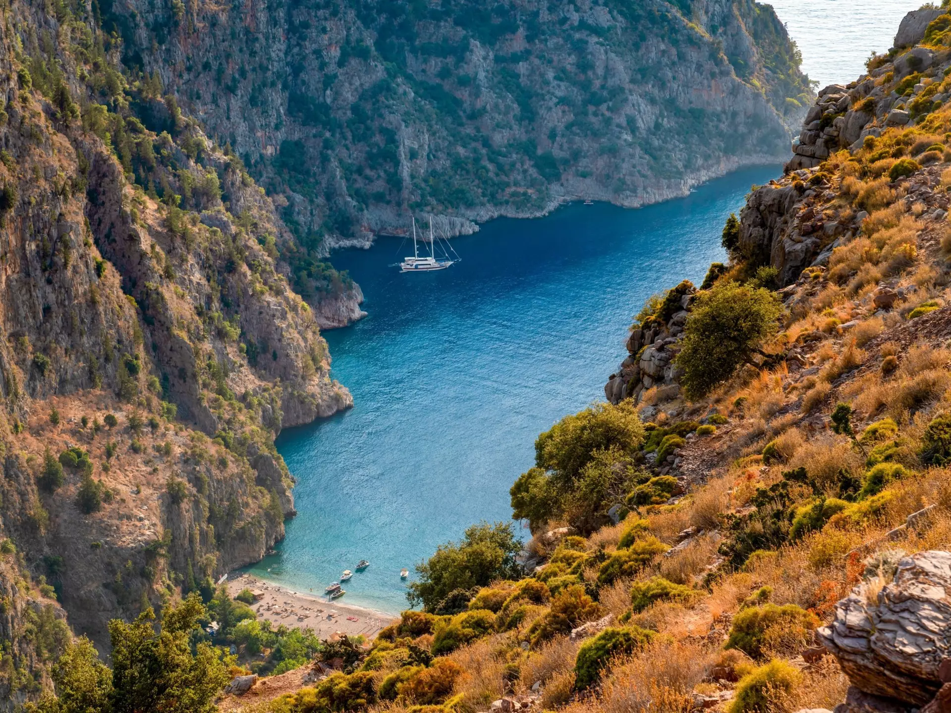 A cove below steep cliffs; boats are docked in blue water.