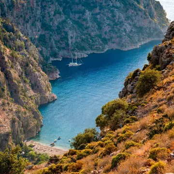 A cove below steep cliffs; boats are docked in blue water.