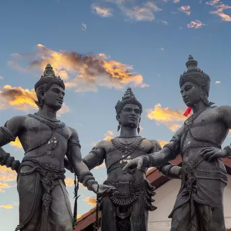 Three statues of Thai kings with clouds lit by sunset in the background. 