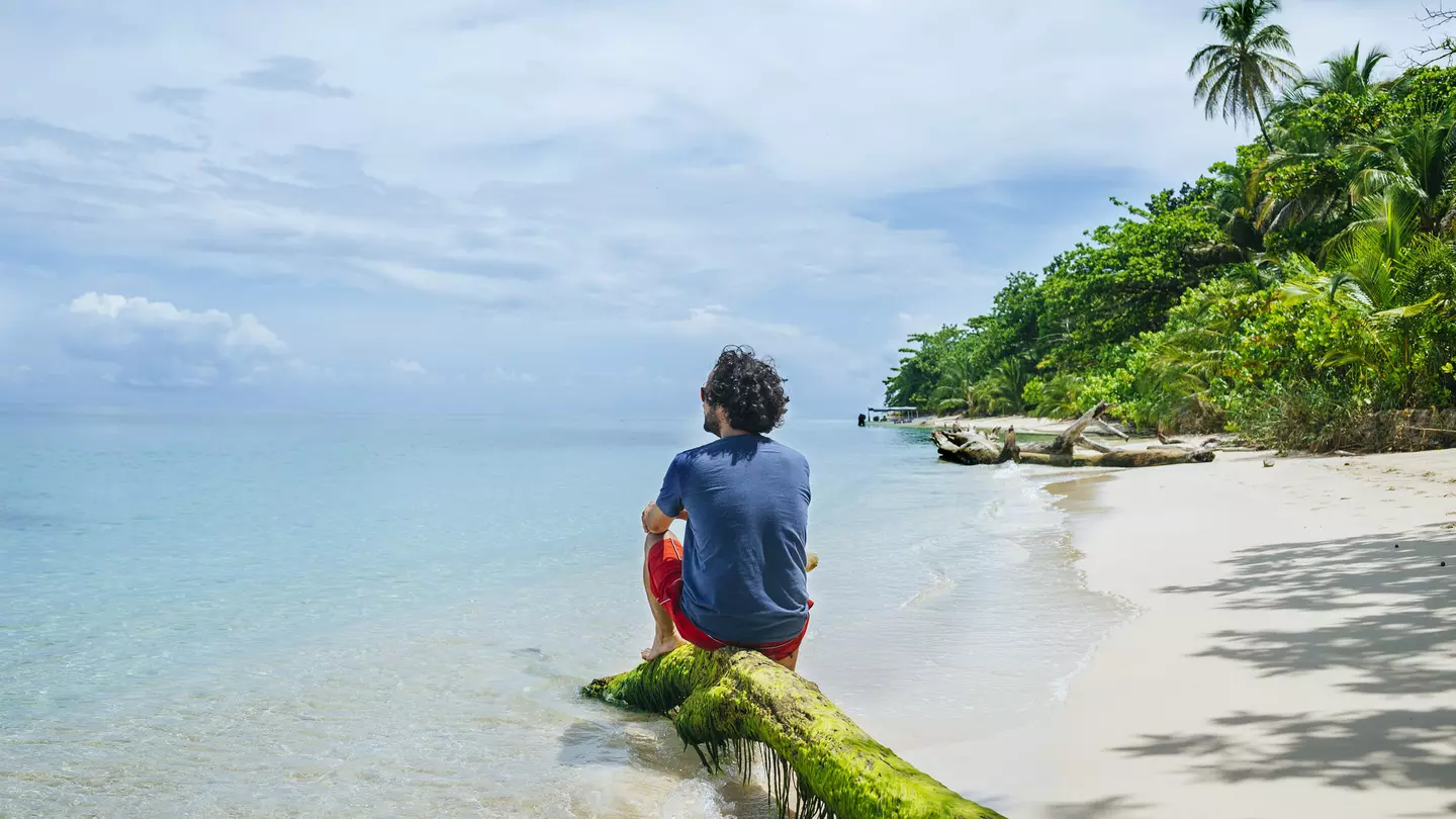 Man sitting on a tree trunk at the beach on Cayo Zapatilla.