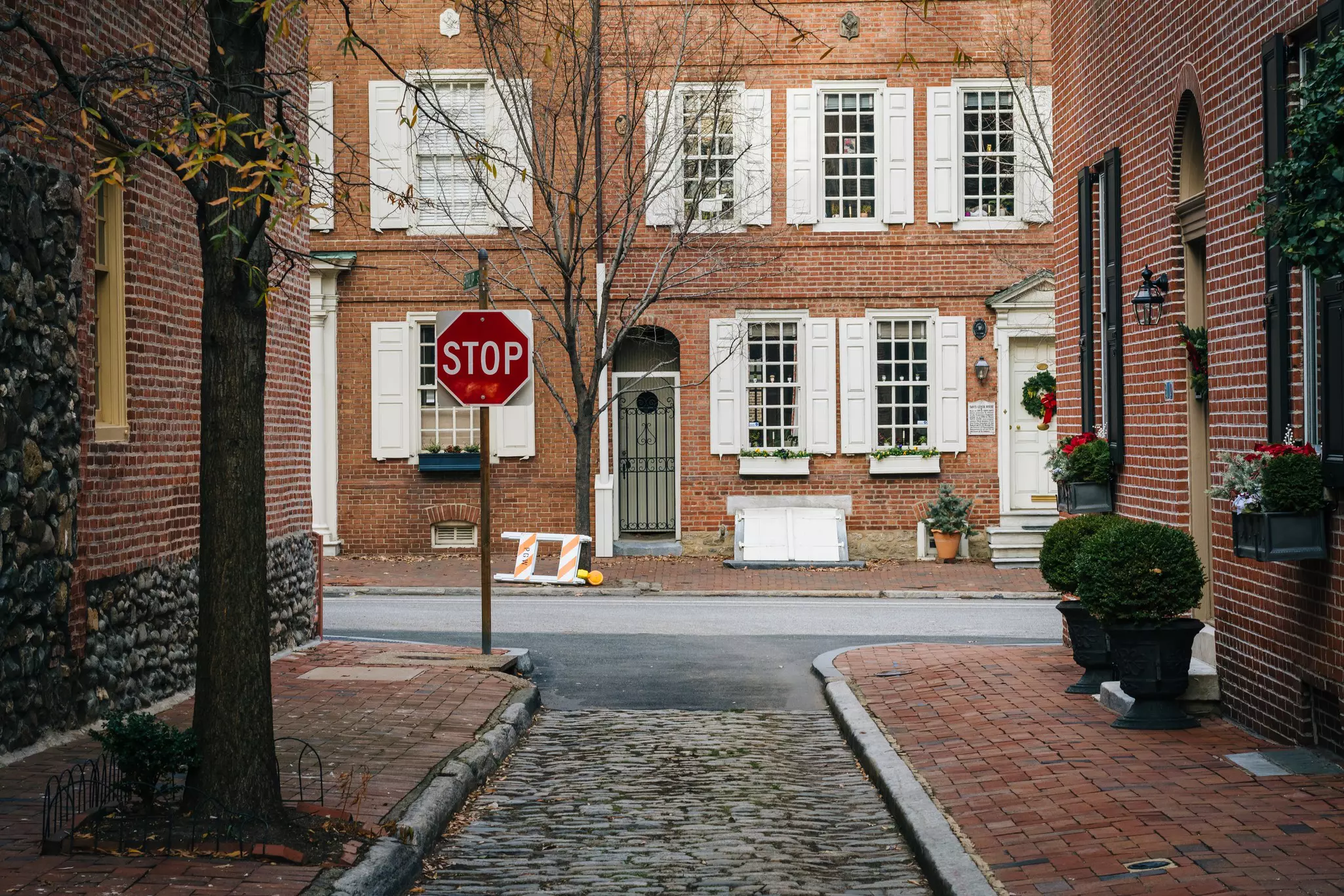 Old red brick row houses near a narrow cobblestone alley with a stop sign at the intersection of the alley and a paved street