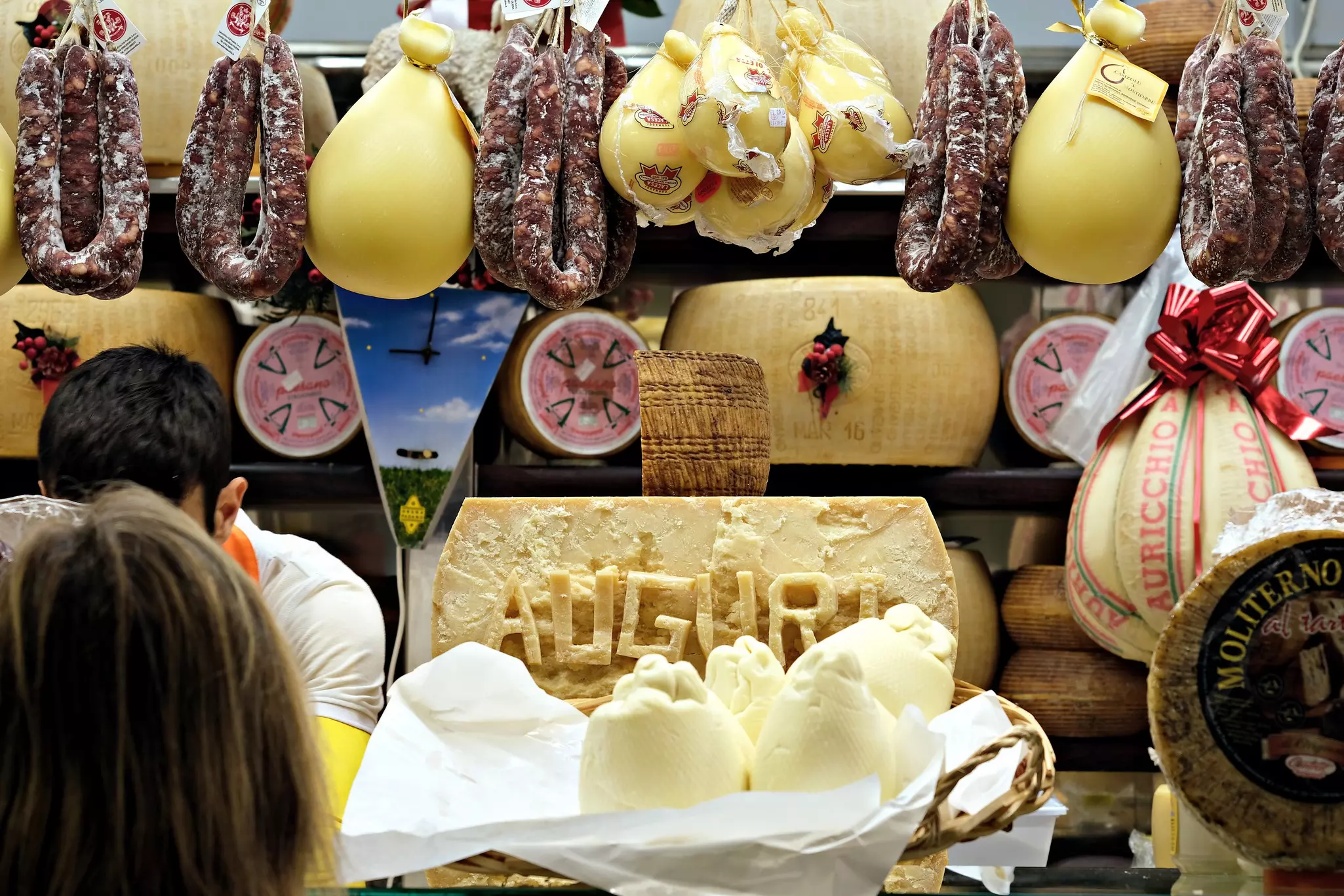 Cheese and cured meats hang on display inside a delicatessen.