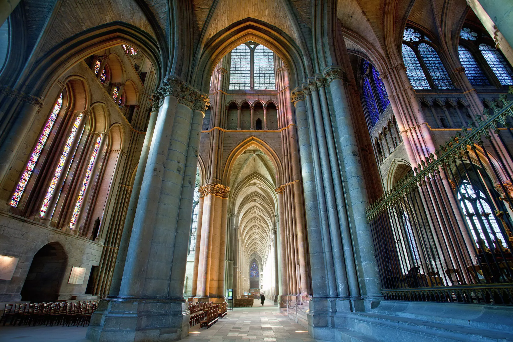 A solo figure wanders through the nave of a vast cathedral with massive stone columns reaching up to a vaulted ceiling.