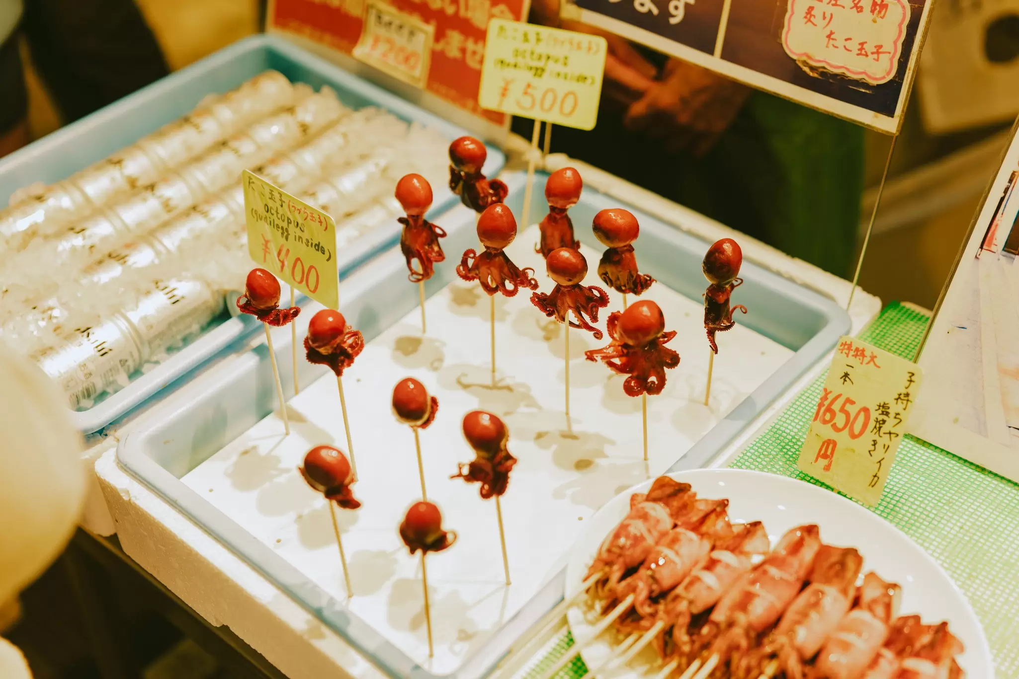 A tray of tiny octopuses on wooden sticks at Japanese market stall.