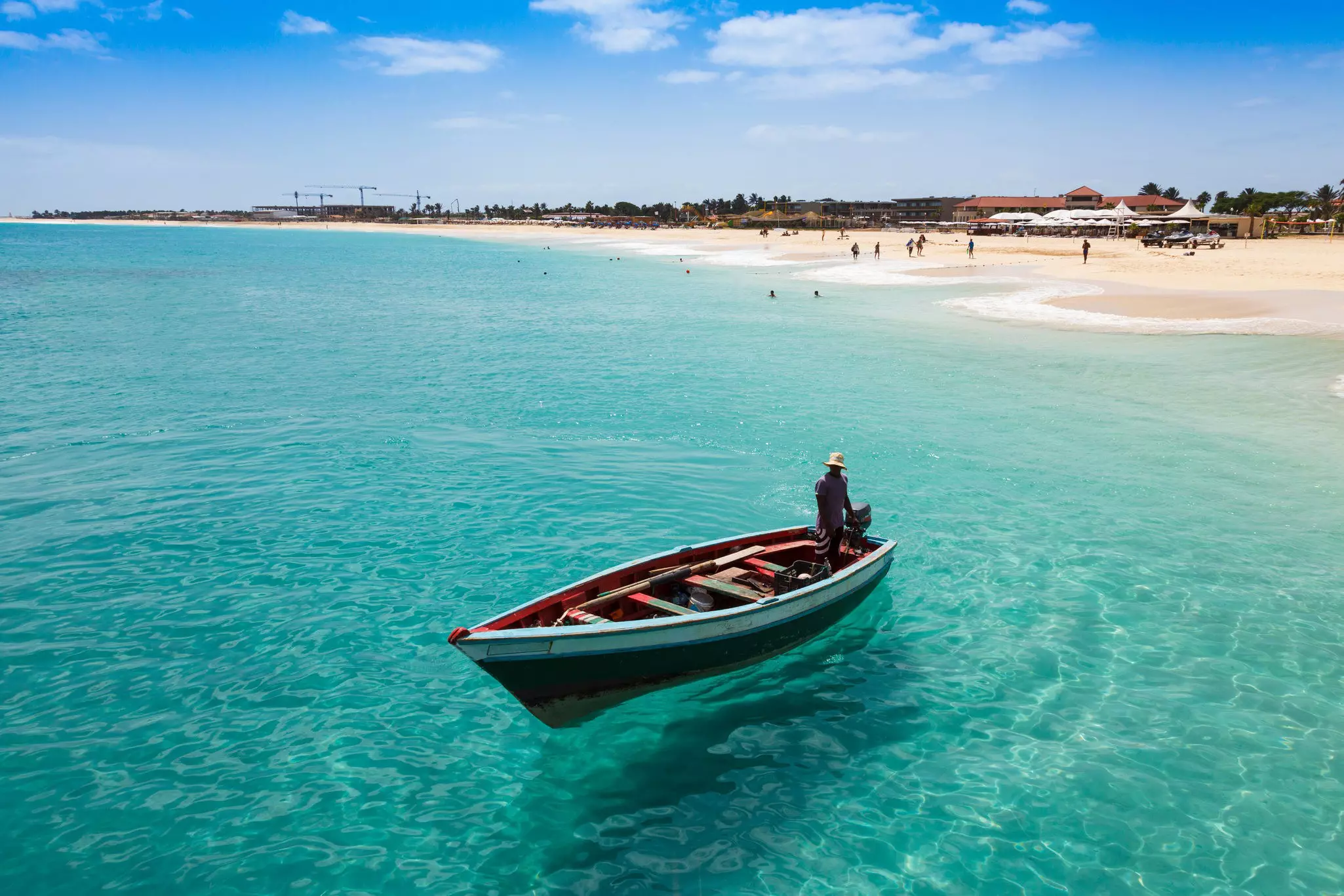 A fishing boat is seen in the shallow azure waters off a wide beach.