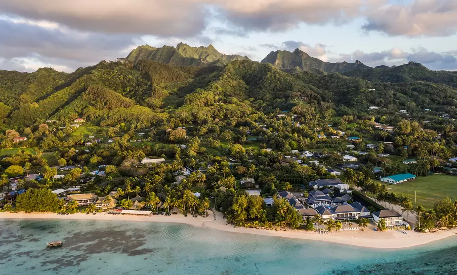 Aerial view of Rarotonga in the Cook Islands: turquoise lagoon, white-sand beach, resorts among palms and jagged green peaks