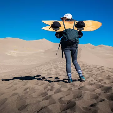 A female holds a sand board at Great Sand Dunes National Park, Colorado, USA