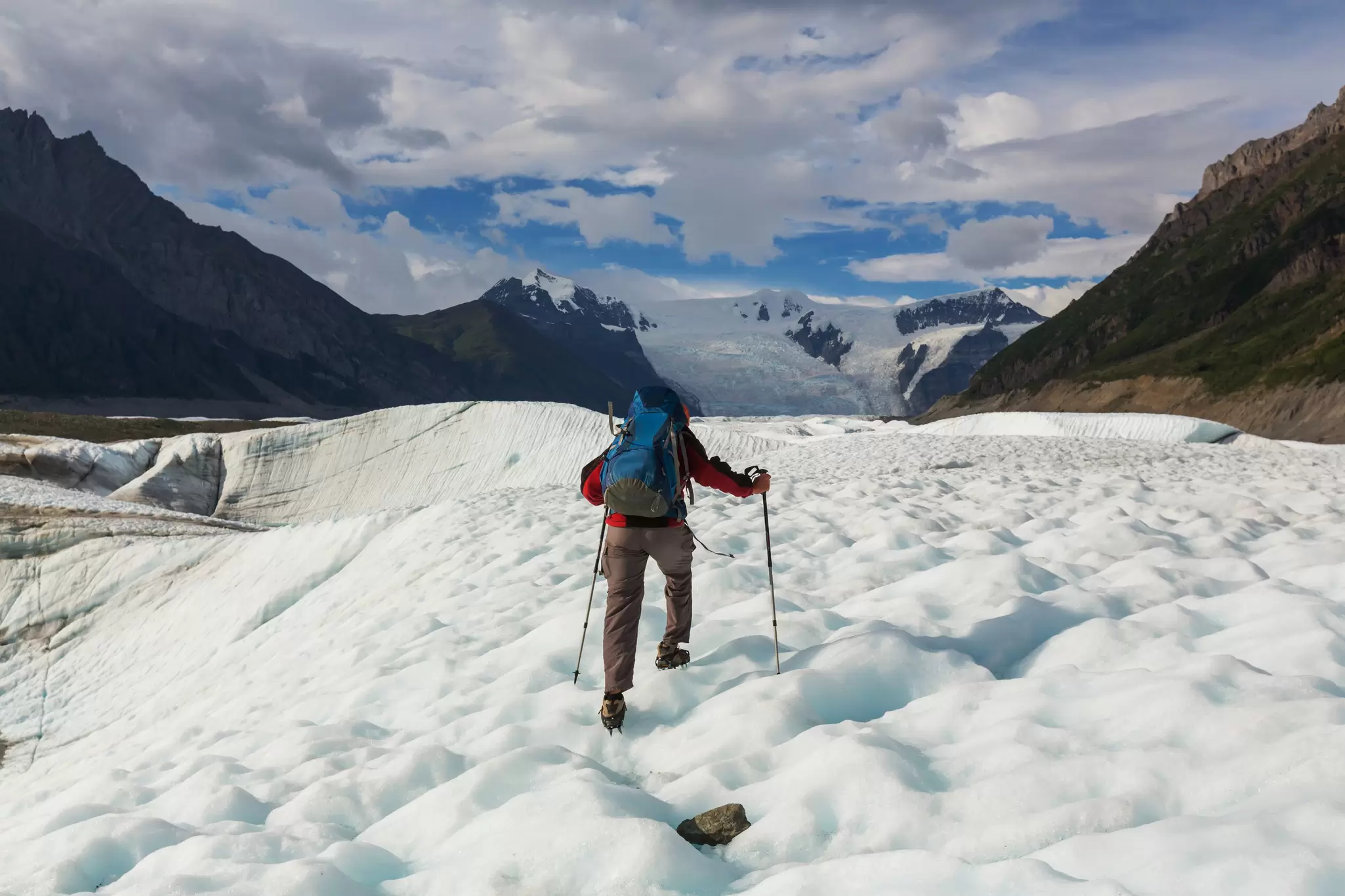 A hiker uses walking sticks to walk on ice.