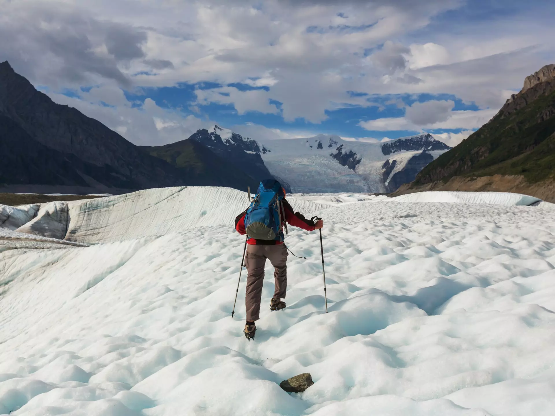 A hiker uses walking sticks to walk on ice.