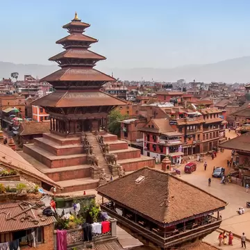 Tall five-roofed brick pagoda on a stepped plinth beside a wide temple and a square with people and brick houses, Bhaktapur.