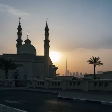A waterside mosque and distant tall skyscraper at sunset: Dubai