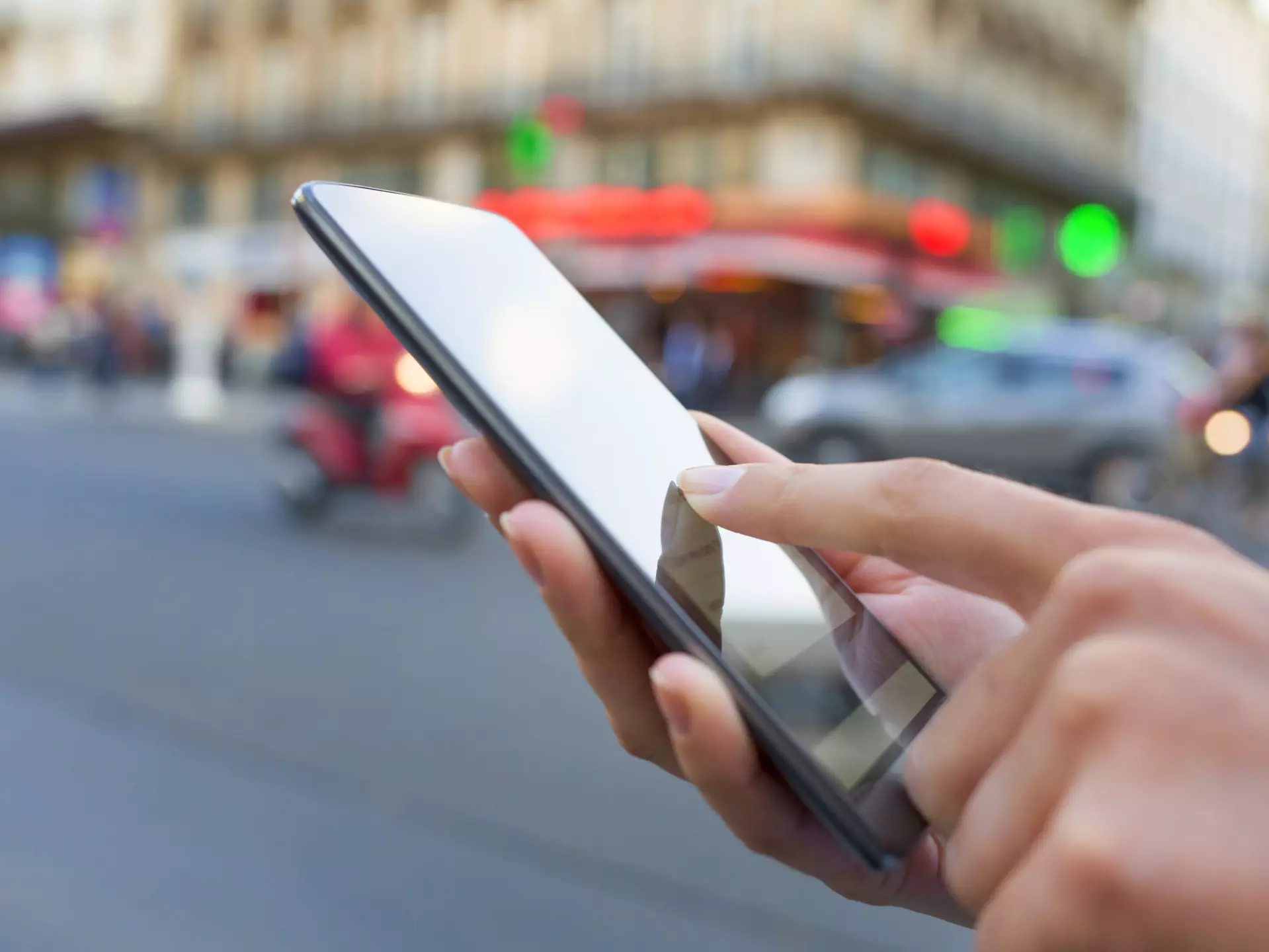 A hand holding a smart phone at a busy street intersection in Paris