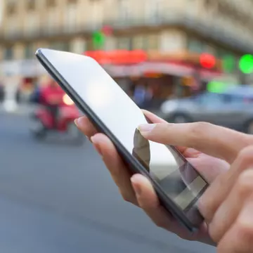 A hand holding a smart phone at a busy street intersection in Paris
