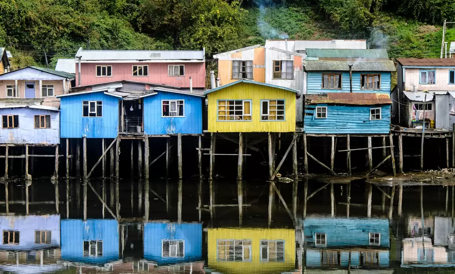 Chiloé's colourful wooden stilt houses (palafitos) in blue, yellow and pink, reflected in still water, Chile