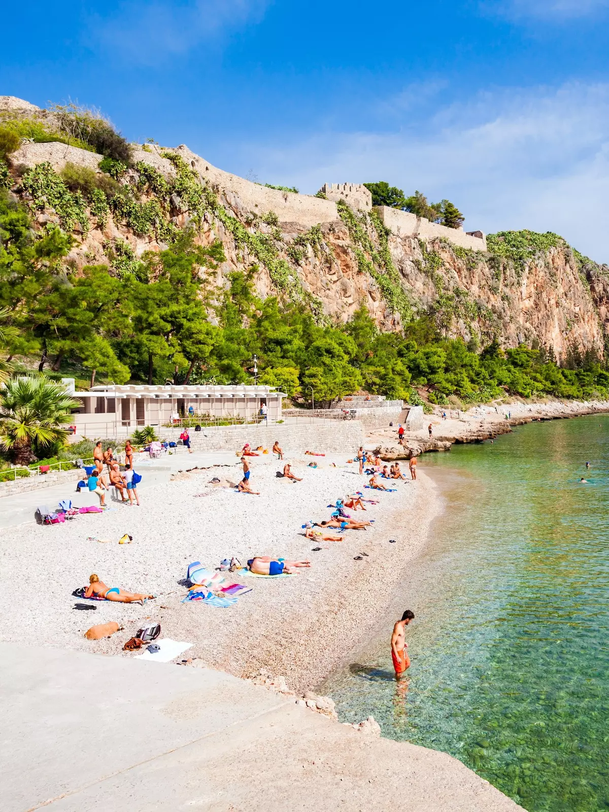 People sunbathe on a white pebbly beach.