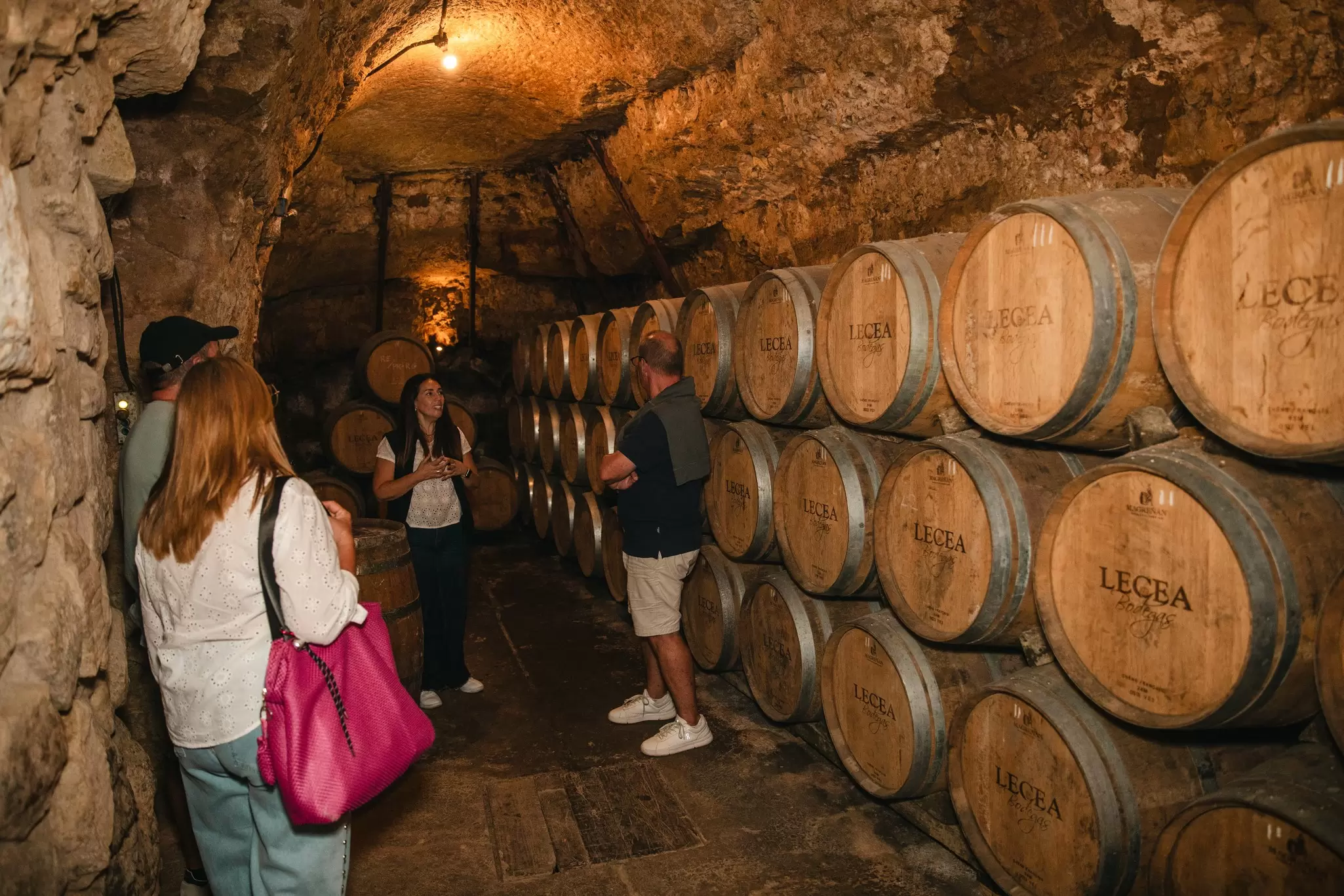 A small group of people in a barrel-lined passageway on a tour of a wine cellar in Bodegas Lecea, Rioja, Spain.