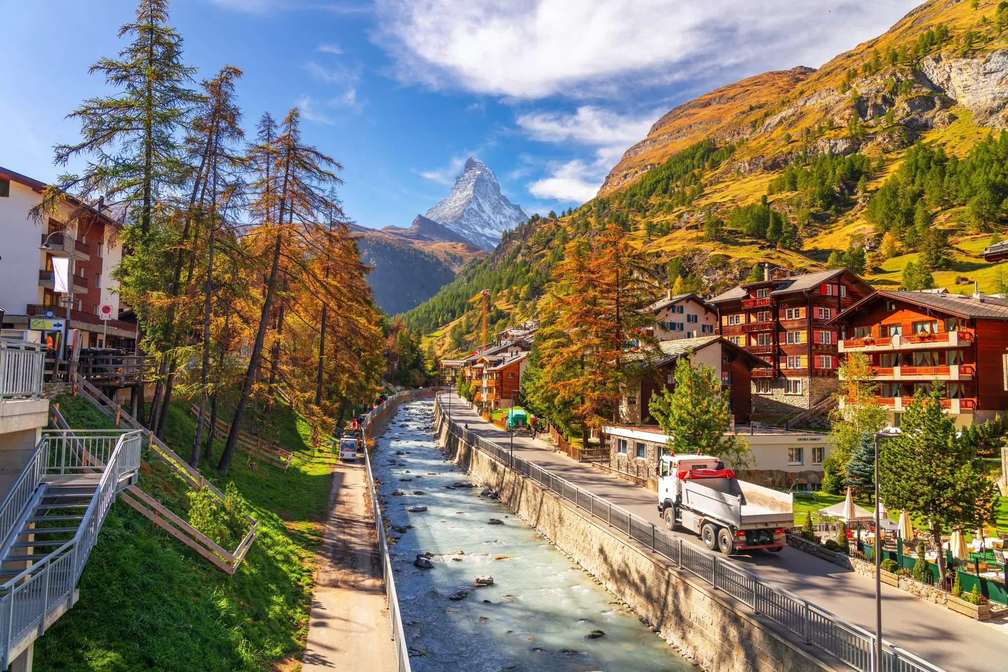 Autumn foliage and rust-colored homes in Zermatt, with a truck cruising by on the local road.