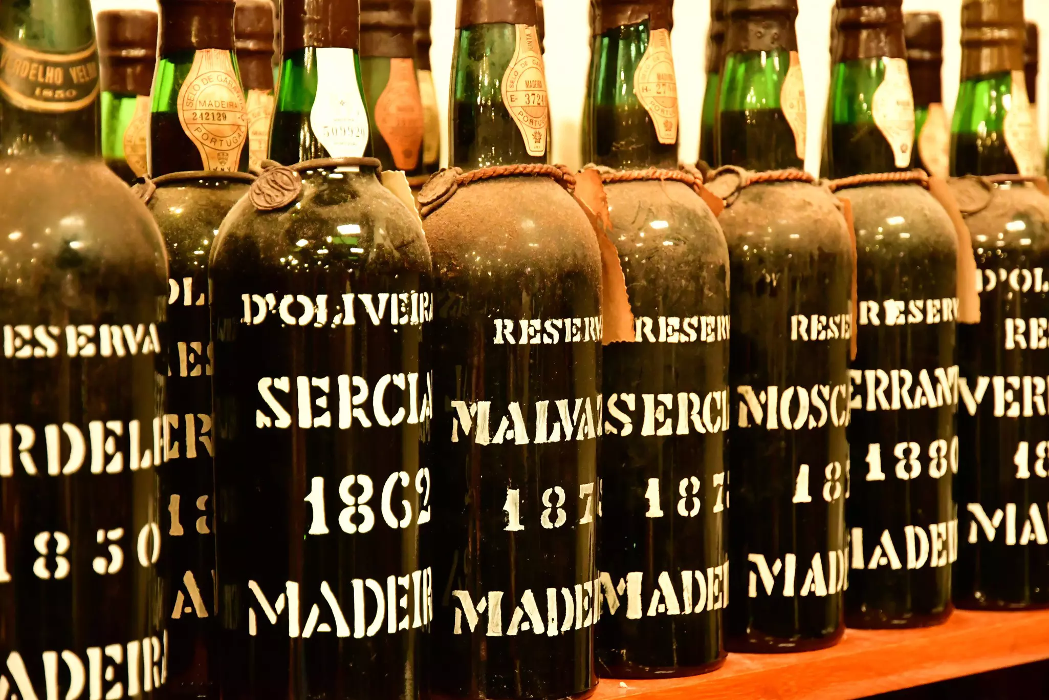 Bottles of wine with hand lettering sit on a shelf in an aging cellar.