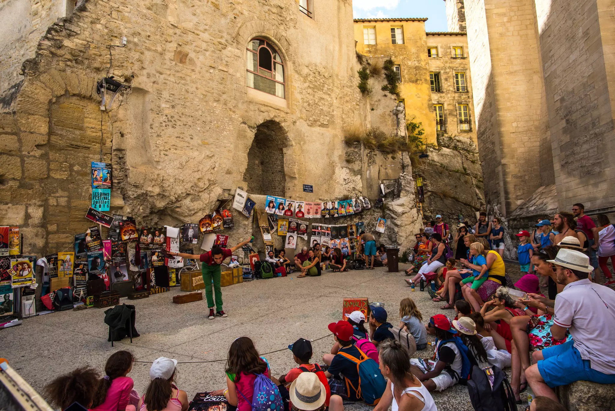 France -- Avignon theatre festival with a performer in a square surrounded by colourfully dressed audience members.