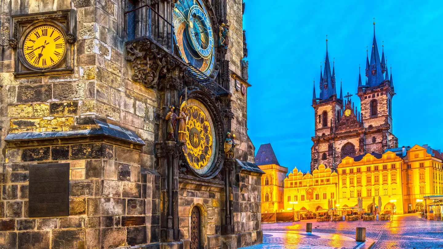 A damp city square in the evening with an ornate astronomical clock in gold and blue