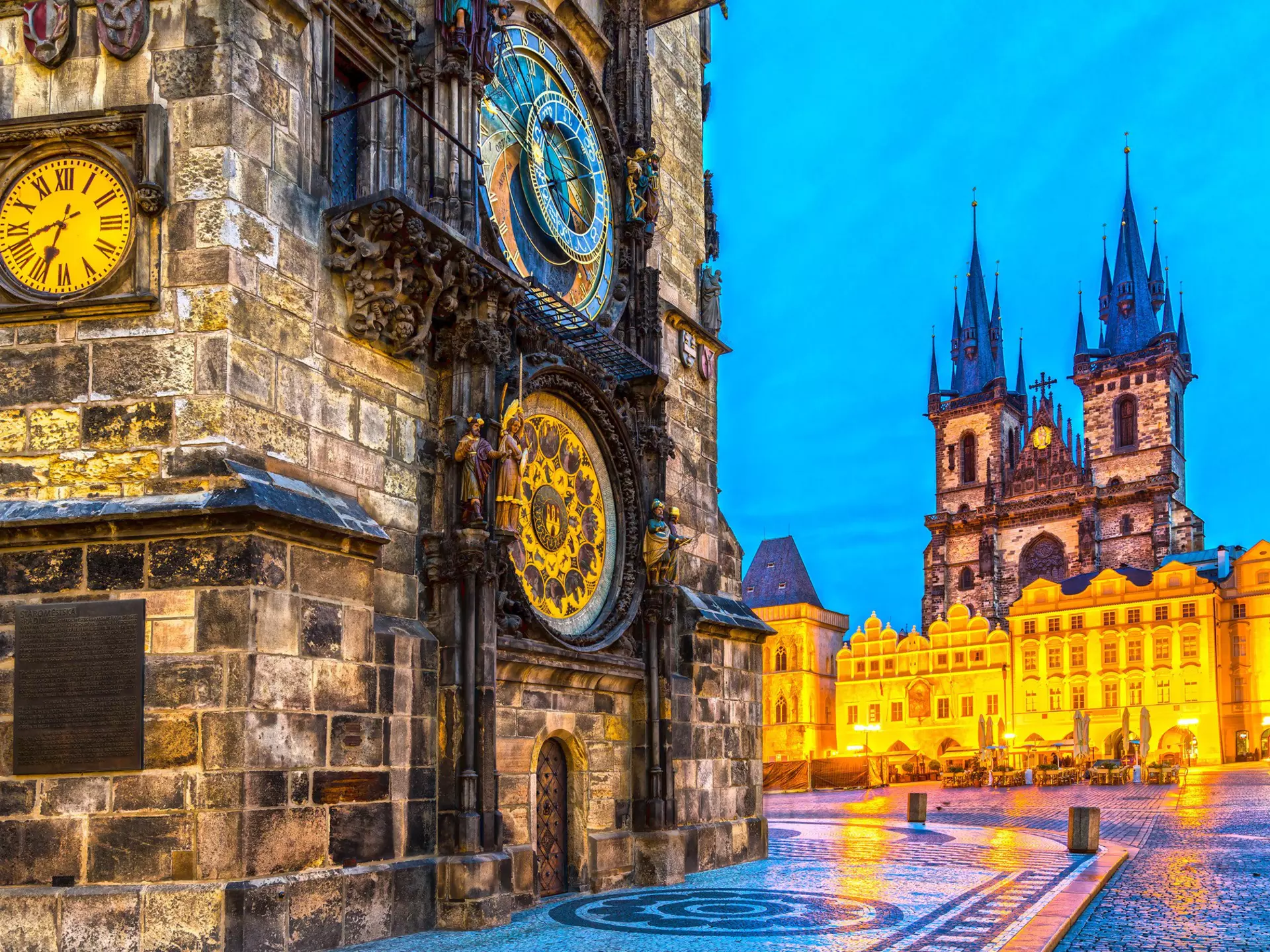 A damp city square in the evening with an ornate astronomical clock in gold and blue