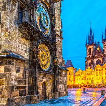 A damp city square in the evening with an ornate astronomical clock in gold and blue