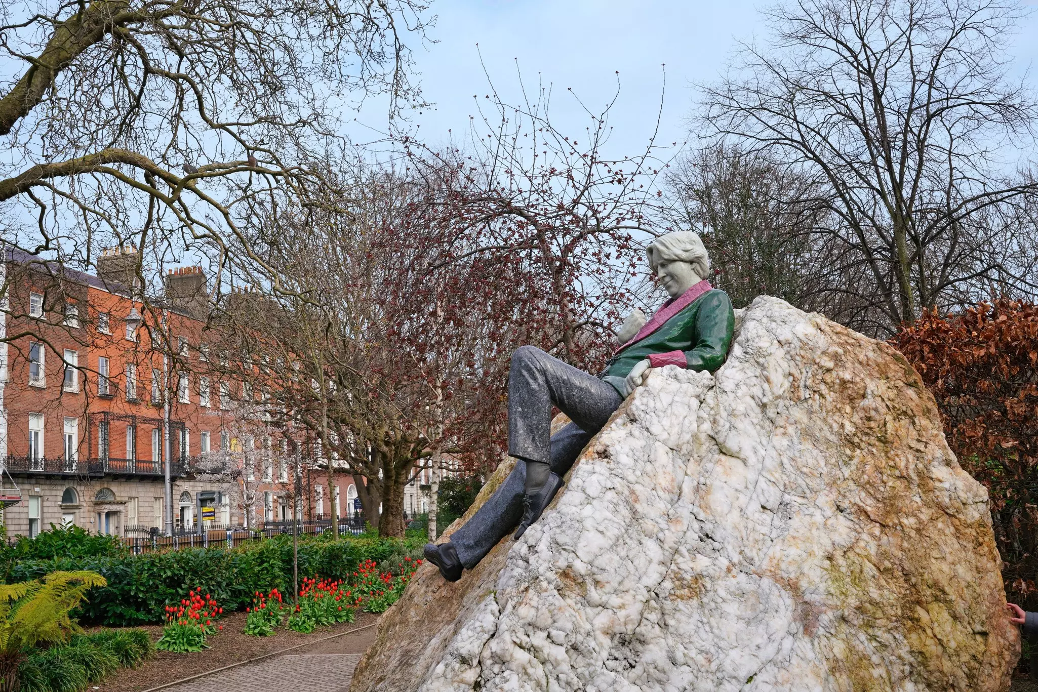 A metal statue of a figure on a rock in a city square is painted bright colors.